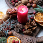 Red candle burning on Yule table with fruit and greenery