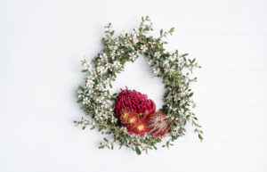 Australian native flower wreath on a white rustic background. Mostly white Tea Tree featuring a Red Waratah, Red Banksia Coccinea and Gum Nut flowers
