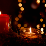 Two candles near holiday tree and sparkling lights