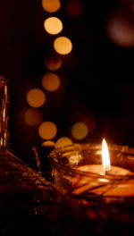Two candles near holiday tree and sparkling lights