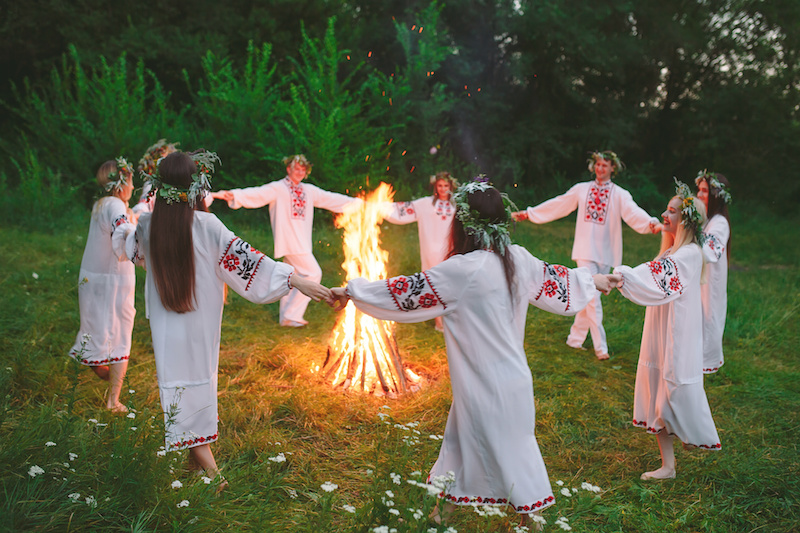 young people in Slavic clothes circle dance around a bonfire in the forest