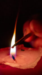 Hand lighting a candle and candlelight in the darkness with Advent wreath