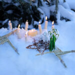 altar for Imbolc sabbath, pagan holiday ritual. Brigid's cross of straw, candles, snowdrops, toy sheep on snow, winter forest natural background. symbol of Imbolc holiday,