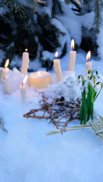 altar for Imbolc sabbath, pagan holiday ritual. Brigid's cross of straw, candles, snowdrops, toy sheep on snow, winter forest natural background. symbol of Imbolc holiday,