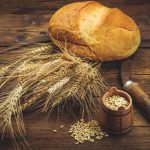 Wheat grain scythe seeds and bread on wooden table