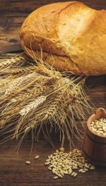 Wheat grain scythe seeds and bread on wooden table