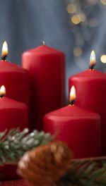 red candles, spruce branches, cones and garland on red table on blurry background.