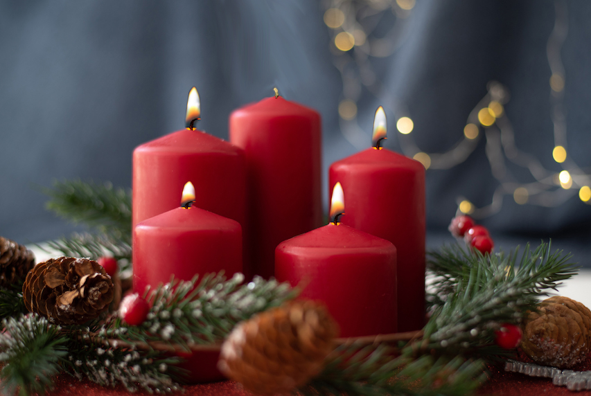 red candles, spruce branches, cones and garland on red table on blurry background.