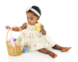 A beautiful baby girl, all dressed up, exploring her first Easter basket. On a white background.